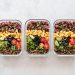 Three glass containers filled with rice, corn, olives, tomatoes, cucumbers, and lentils